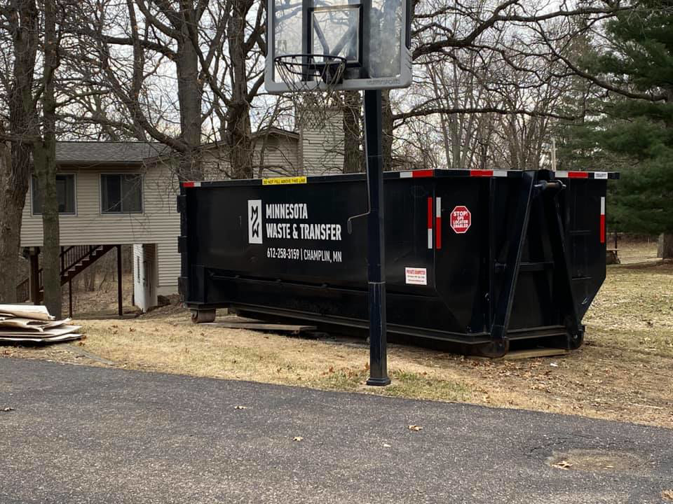 A large junk removal dumpster from Minnesota Waste and Transfer placed in a residential yard in Champlin, MN