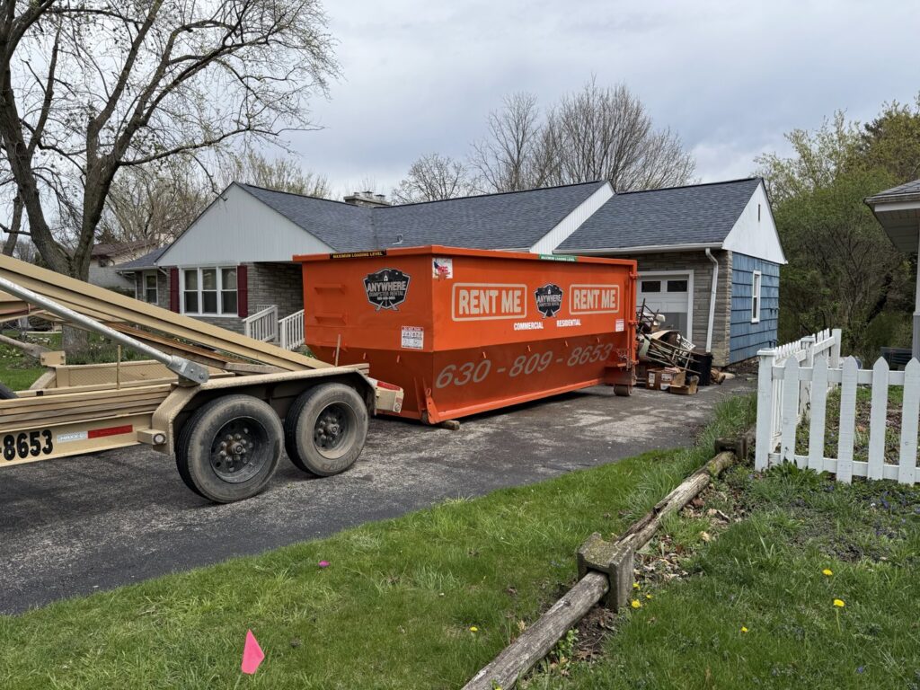 A roll-off dumpster being loaded onto a truck after a junk removal job by Anywhere Dumpster Rental in Bolingbrook Area, IL.