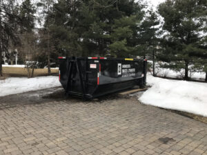 A large black junk removal dumpster from Minnesota Waste and Transfer placed on a paved driveway in Champlin, MN during winter