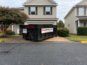 A black dumpster from The Junk Ninjas placed in a residential driveway for junk removal in Hampton Roads, VA.