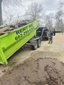 A bright green dumpster full of construction debris being unloaded by Tristate Dumpsters LLC in Greenville, MS.