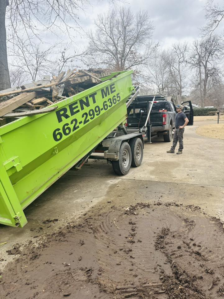 A bright green dumpster full of construction debris being unloaded by Tristate Dumpsters LLC in Greenville, MS.