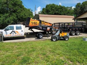 Junk removal equipment including a truck, dumpster, and skid steer loader from Dump My Junk LLC Demolition & Dumpster Rental in Tampa, FL.