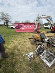 Junk removal job with a pink dumpster and excavator clearing debris by Dump It in Middletown, DE
