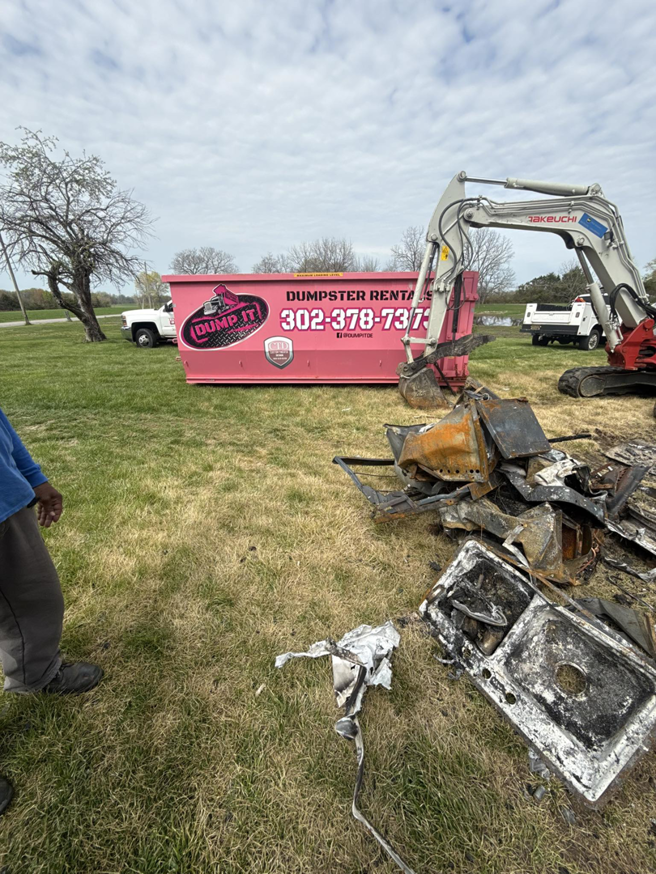 Junk removal job with a pink dumpster and excavator clearing debris by Dump It in Middletown, DE
