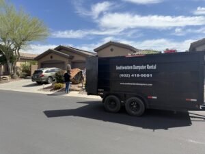 A person near a black dumpster trailer from Southwestern Dumpster Rental and Junk Removal, with a large item like a hot tub nearby, indicating a junk removal job in Peoria, AZ.