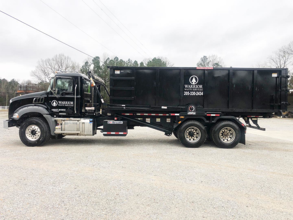A black junk removal roll-off truck with a large dumpster from Warrior Waste Services in Northport, AL.