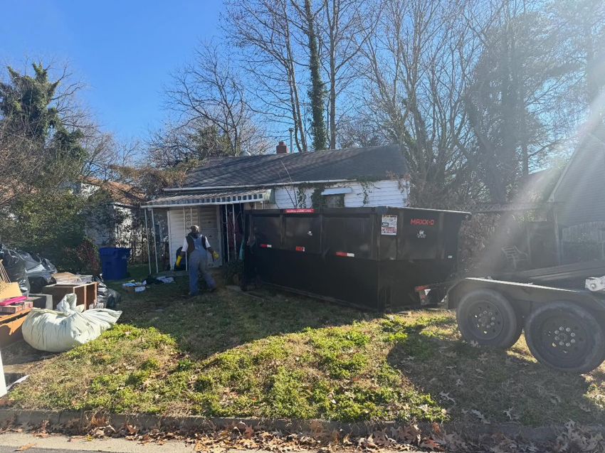 A worker performing junk removal services with a black dumpster from Great Bridge Bins, LLC in Chesapeake, VA.