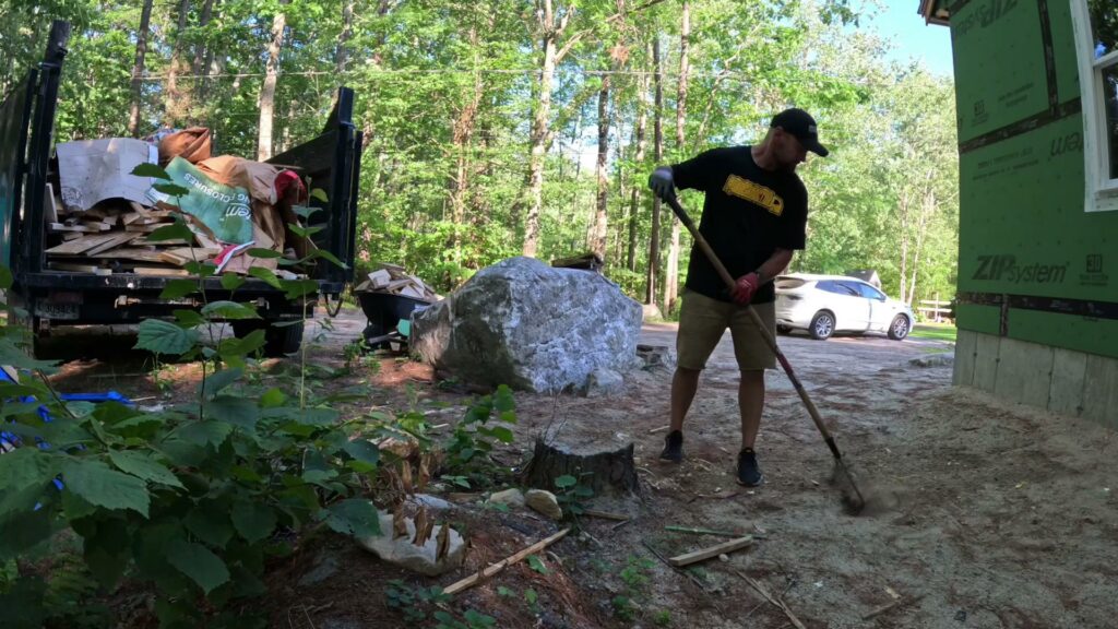 A Rubbish Doctor employee cleaning up a site with a shovel, with a junk removal truck in the background in Portland, ME.