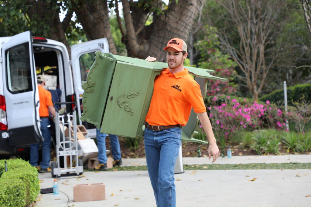 A The Junkiez Junk Removal specialist carrying a green cabinet on his shoulder in Los Angeles, CA.