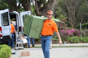 A The Junkiez Junk Removal specialist carrying a green cabinet on his shoulder in Los Angeles, CA.