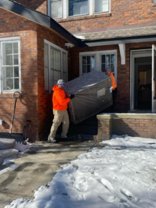 A junk removal team carrying a large item down the steps of a house for In & Out Junk Removal Service LLC in Chicago, IL.