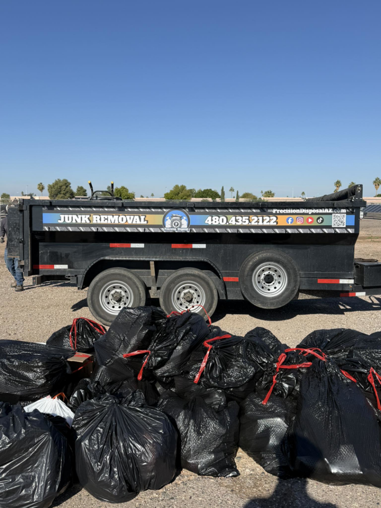 A junk removal trailer parked next to a large pile of black trash bags, ready for disposal by Precision Disposal in Port Saint Lucie, FL.