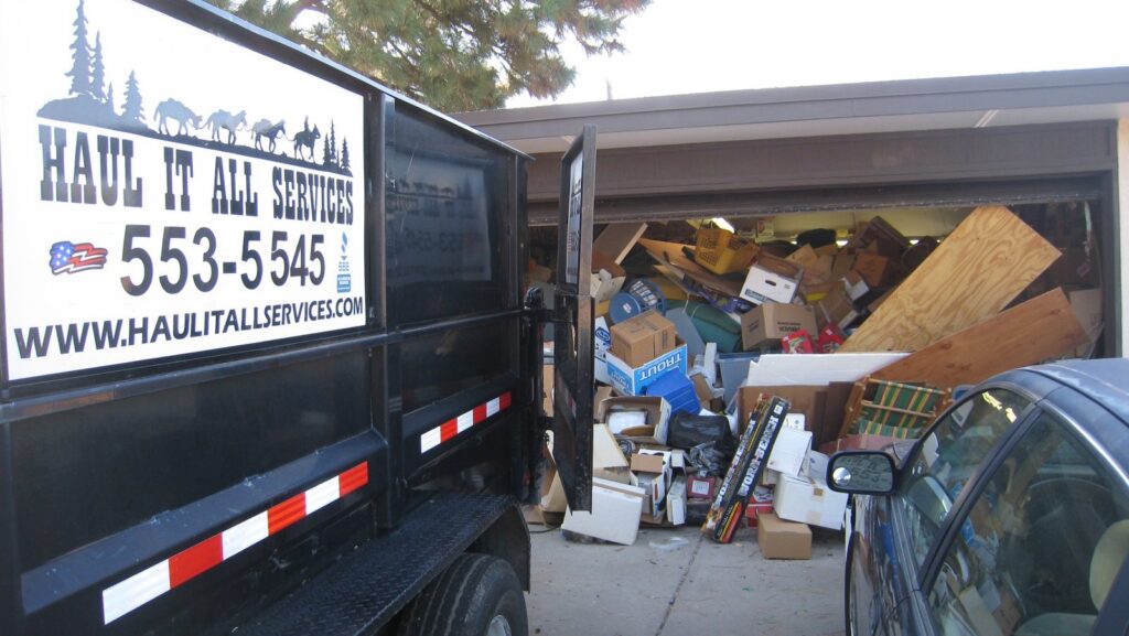 A Haul It All Services junk removal trailer parked in front of a garage overflowing with household junk in Albuquerque, NM