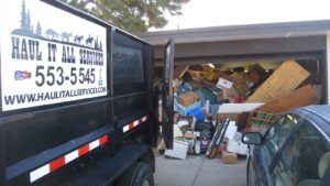 A Haul It All Services junk removal trailer parked in front of a garage overflowing with household junk in Albuquerque, NM