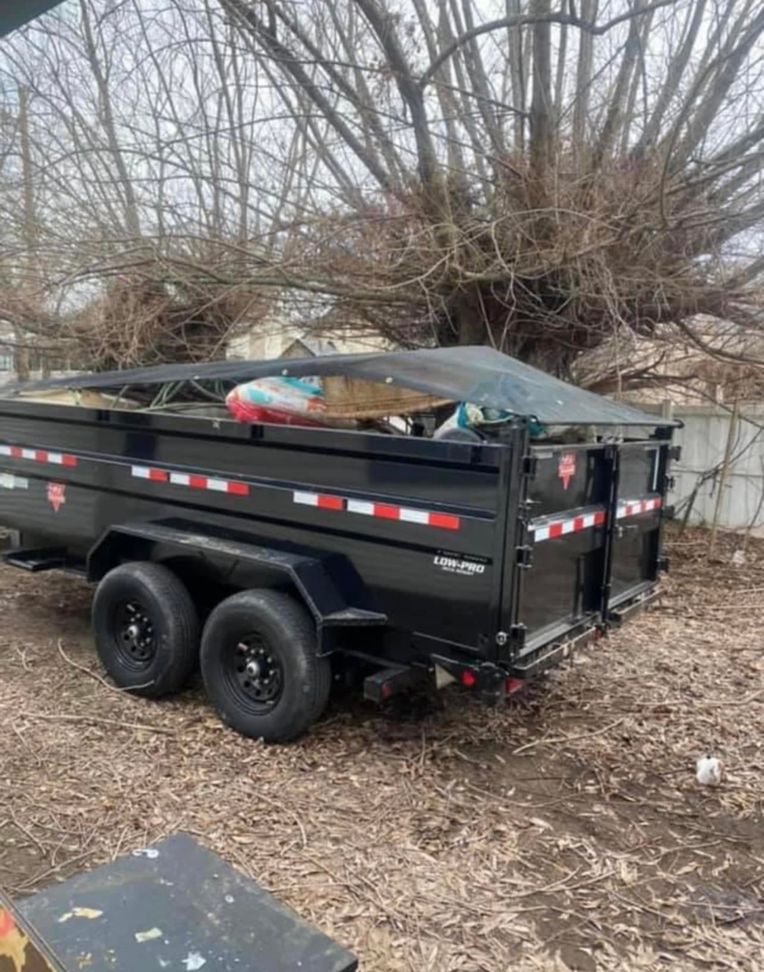 A black junk removal trailer with a protective tarp covering loaded items, provided by S&J Rental and Removal in Ogden, UT.