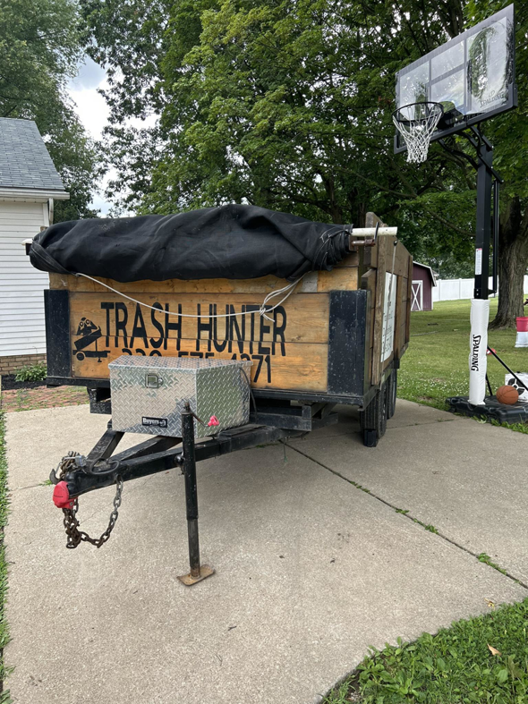 A Trash Hunter LLC junk removal trailer with wooden sides and a tarp cover parked on a driveway in Hartville, OH.