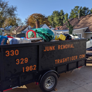 A trash_tiger junk removal trailer filled with debris and household items, parked in a residential area in Canton, OH.
