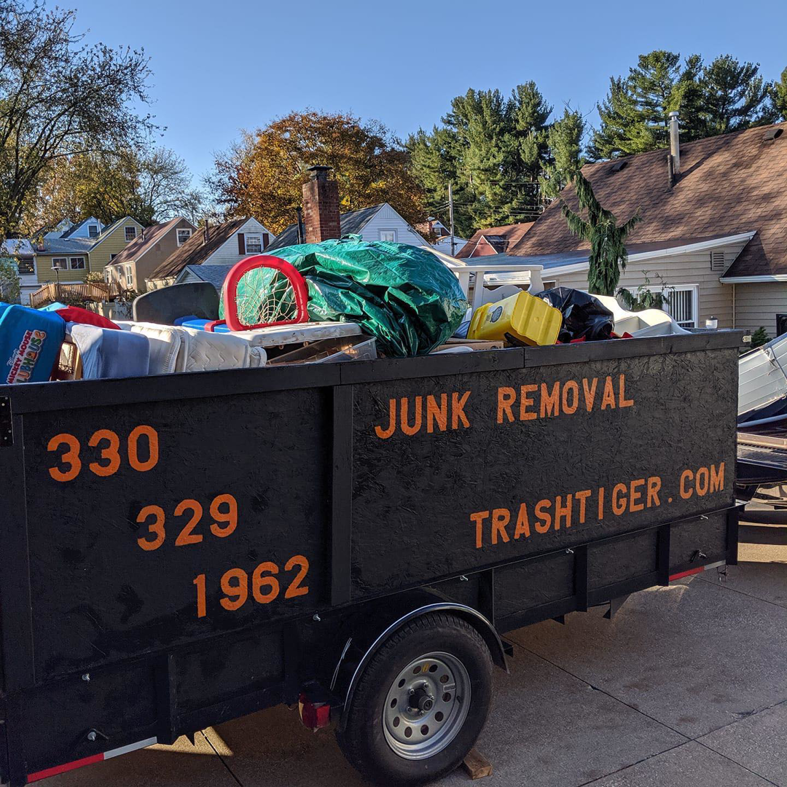 A trash_tiger junk removal trailer filled with debris and household items, parked in a residential area in Canton, OH.