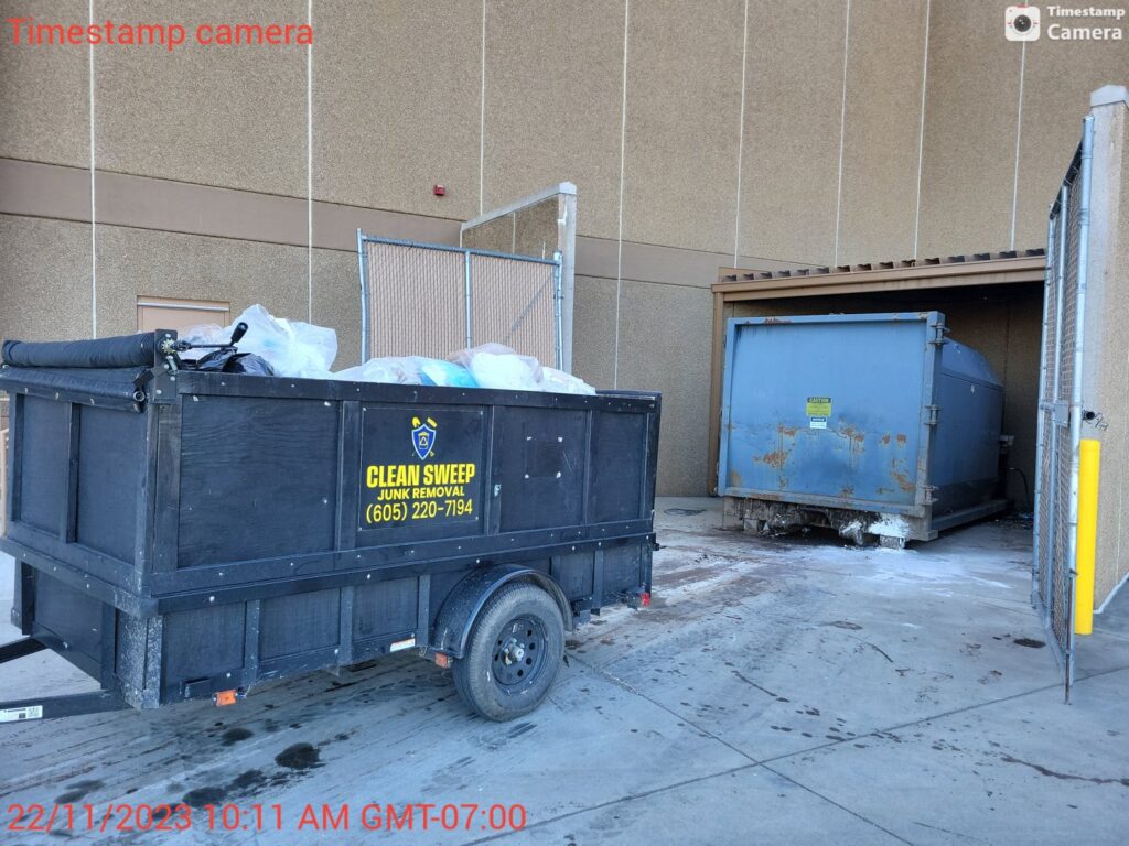 A Clean Sweep Junk Removal trailer full of trash bags and debris at a commercial site in Augusta, ME.