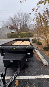 A black dump trailer partially loaded with cardboard boxes and covered with a tarp for 614junkremoval in Columbus, OH.