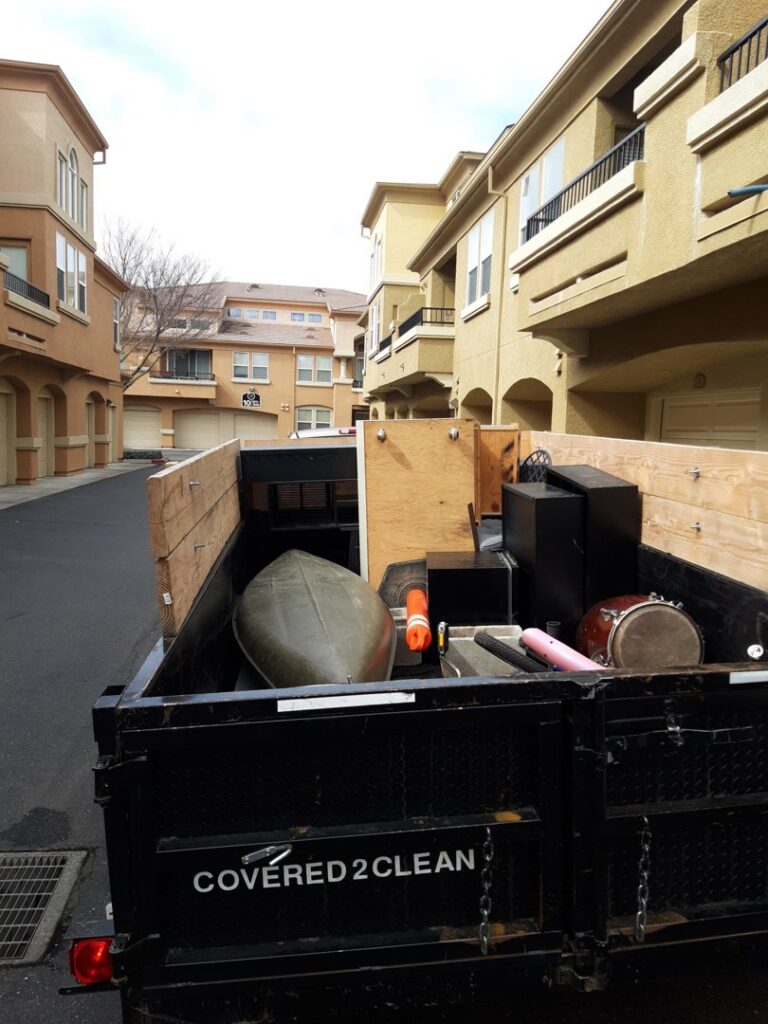 A Covered2Clean junk removal/hauling trailer loaded with various items, including a canoe, in Sacramento, CA.