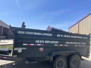 A junk removal trailer, partially loaded with debris, displaying JB'S Junk Removal branding in Justin, TX.