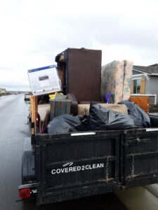 A Covered2Clean junk removal/hauling trailer loaded with a mattress, furniture, and trash bags in Sacramento, CA.