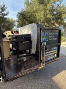 A junk removal trailer from Lightning Bay Junk Removal in Tampa, FL, loaded with a grill, mattress, and other household debris.