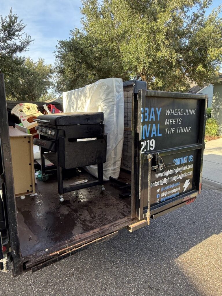 A junk removal trailer from Lightning Bay Junk Removal in Tampa, FL, loaded with a grill, mattress, and other household debris.