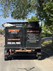 The back of a SpudCity Dumpsters junk removal trailer on a road, showing services offered in Caldwell, ID.