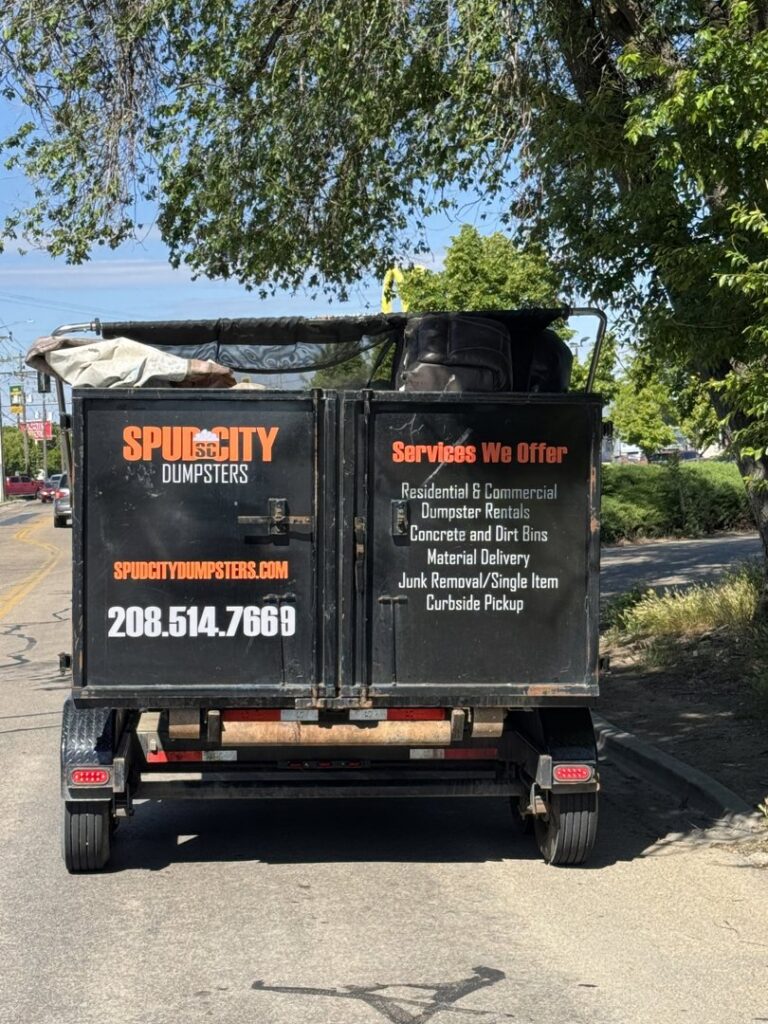 The back of a SpudCity Dumpsters junk removal trailer on a road, showing services offered in Caldwell, ID.