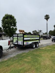 A We-Haul Junk Removal trailer, branded with the company logo, partially loaded with debris in Long Beach, CA
