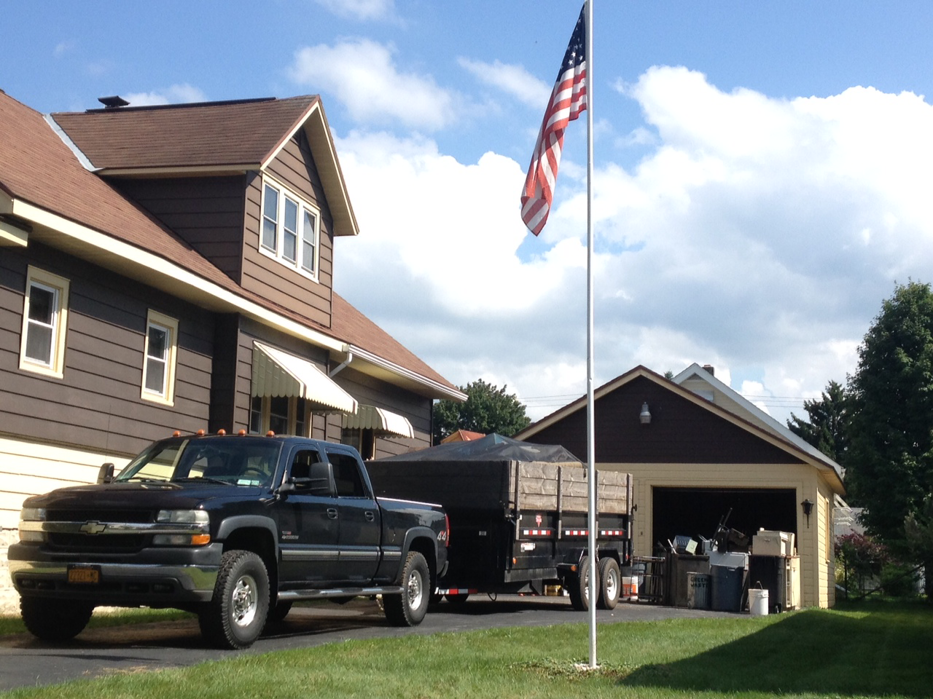 A pickup truck with a full junk removal trailer parked in a driveway by Scott's Utica Junk Removal in New Hartford, NY.