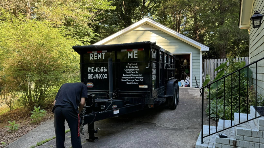 A team member from The Dump Bros LLC setting up a junk removal trailer in a driveway in Raleigh, NC.
