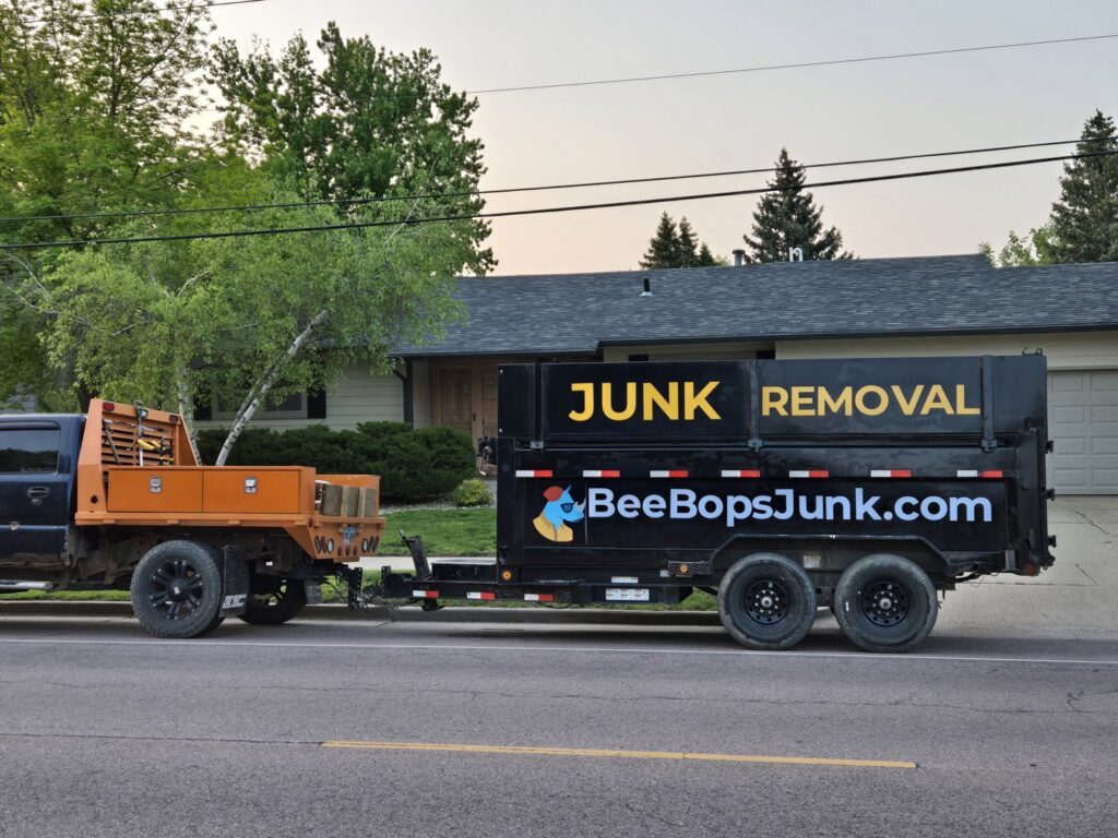 A BeeBop's Junk Removal truck and branded trailer parked on a street in Sioux Falls, SD, ready for a job.