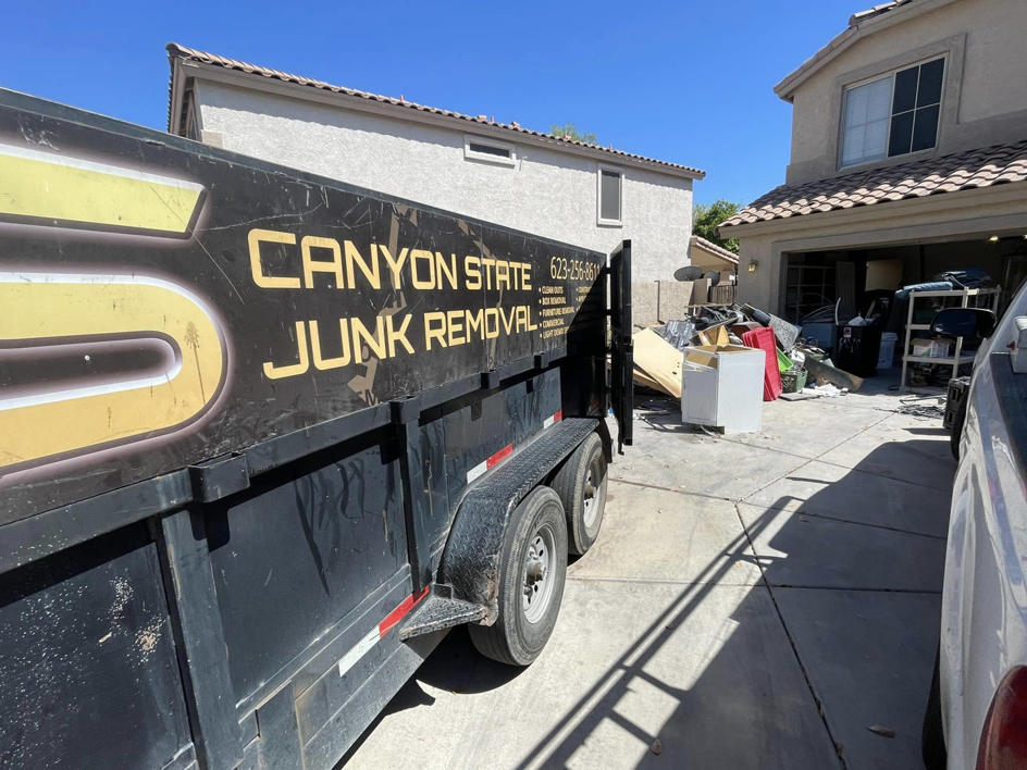 A Canyon State Junk Removal trailer filled with debris parked in a driveway in Peoria, AZ, ready for transport