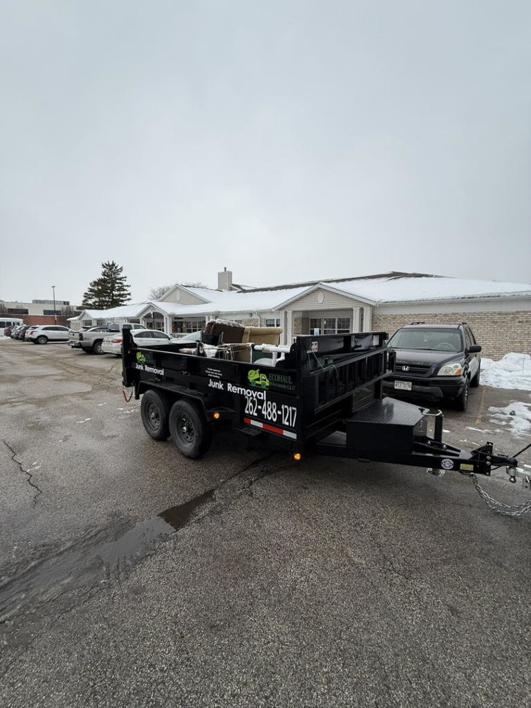 A black junk removal trailer with items inside, branded for EcoHaul Wisconsin LLC, parked in Union Grove, WI.
