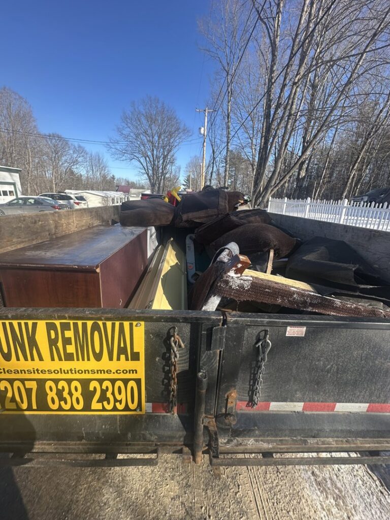 A junk removal trailer with a visible 'JUNK REMOVAL' sign, loaded with various items by CleanSite Solutions in Windham, ME.
