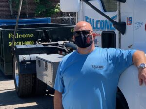 A Falcone Enterprises team member stands next to a junk removal truck and dumpster in Worcester, MA.