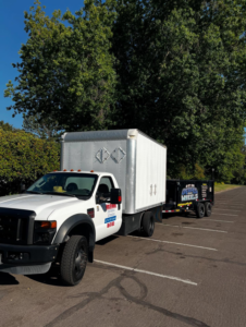 A Debris On Wheels branded white truck pulling a black dump trailer in Eugene, OR.