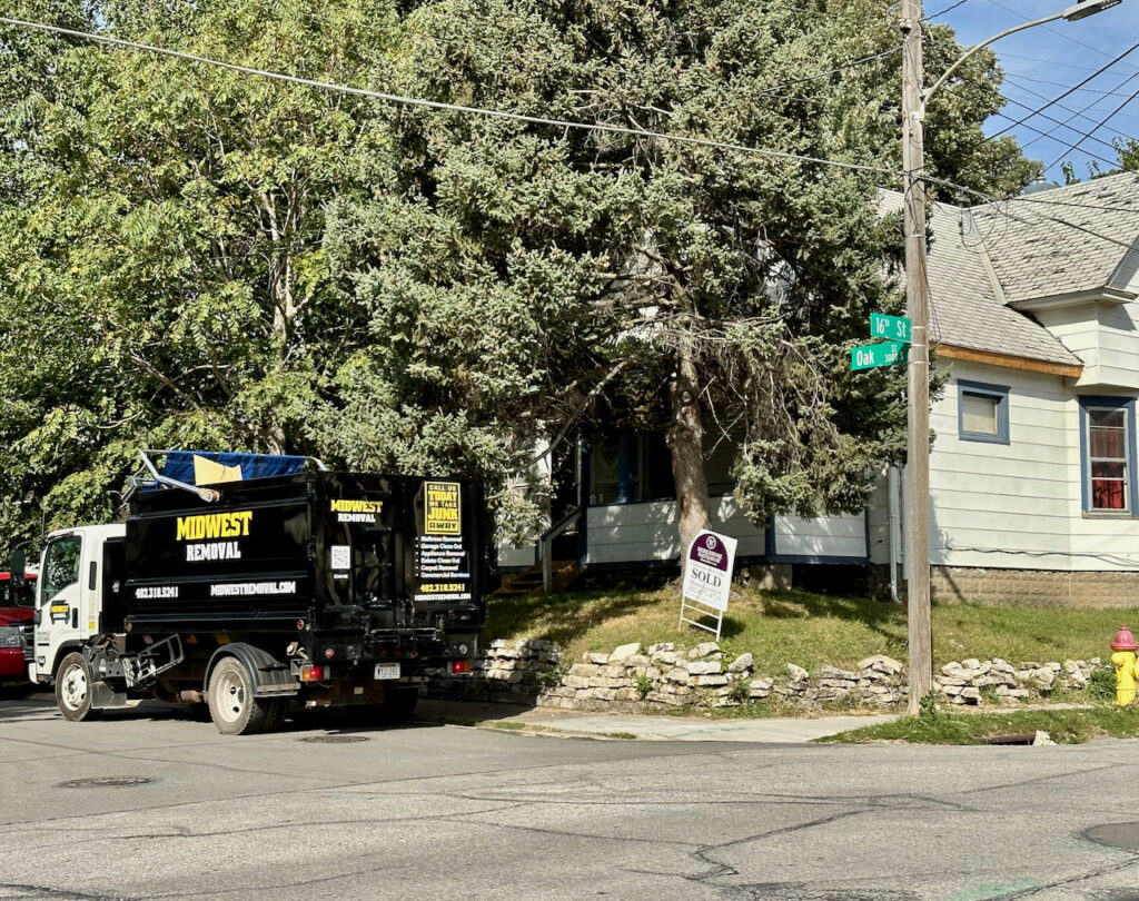 A Midwest Removal truck parked outside a house with a 'SOLD' sign, suggesting an estate cleanout service in Omaha, NE.