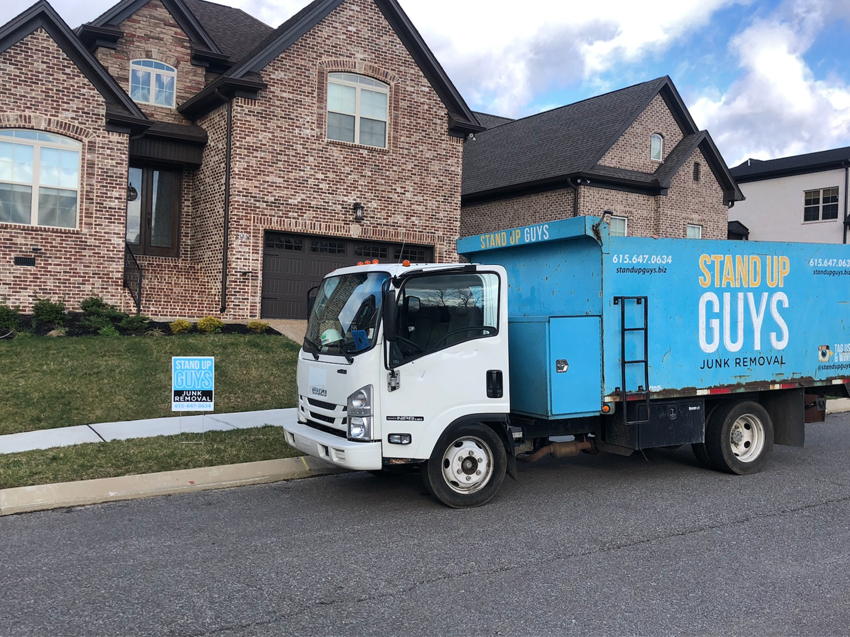 A Stand Up Guys Junk Removal truck parked on the street in front of a brick residential home in Nashville, TN.
