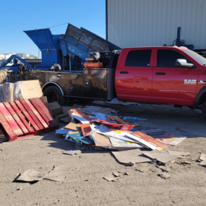 A red junk removal truck next to a pile of cardboard and wooden pallets at a Premier Service job site in North Las Vegas, NV.