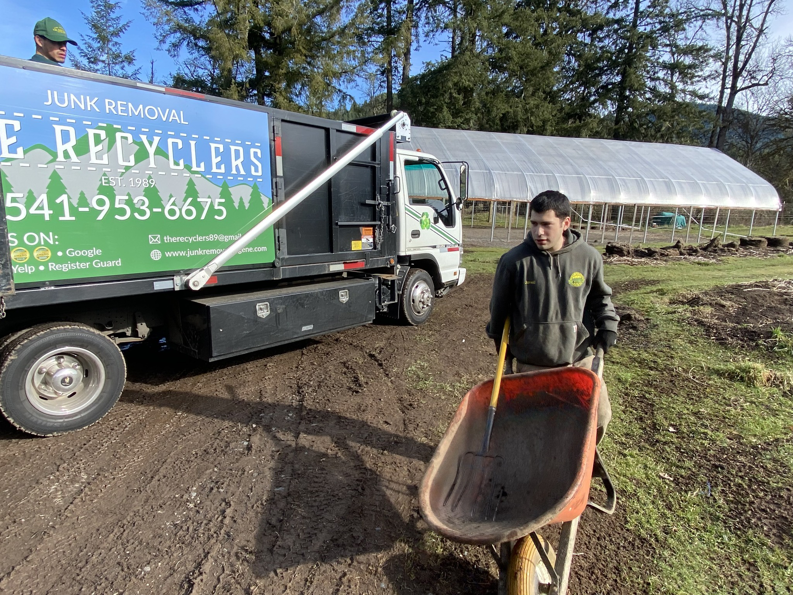 A branded junk removal truck and a crew member with a wheelbarrow from The Recyclers, LLC Junk Removal in Springfield, OR.