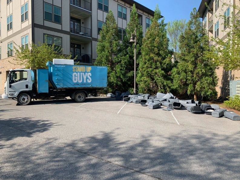 A Stand Up Guys Junk Removal truck parked next to a pile of debris in a parking lot in Nashville, TN.