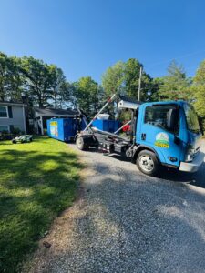 A Barkers Junk Removal & Hauling LLC truck deploying a blue roll-off dumpster in a residential yard in Roanoke, VA.