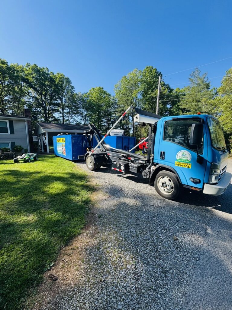 A Barkers Junk Removal & Hauling LLC truck deploying a blue roll-off dumpster in a residential yard in Roanoke, VA.