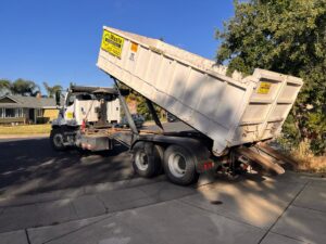 A Waste Removal and Recycling truck deploying a roll-off dumpster on a residential street in Sacramento, CA.