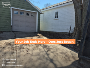 A junk removal truck parked on a driveway next to a garage, ready for service by Siouxland Junk Removal in Sioux City, IA.